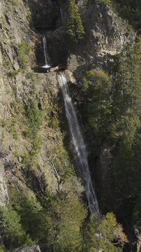 Scenic view of the multi-tiered Los Cesares waterfall cascading down a rugged rocky cliffside surrounded by native forest in Nahuel Huapi National Park, Rio Negro, Argentina.