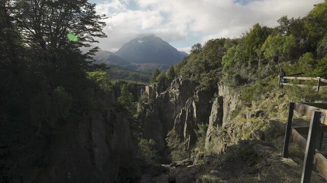 Man standing at a wooden viewpoint overlooking the rocky gorge of Cascada Los Cesares with mountain views in Nahuel Huapi National Park, Rio Negro, Argentina.
