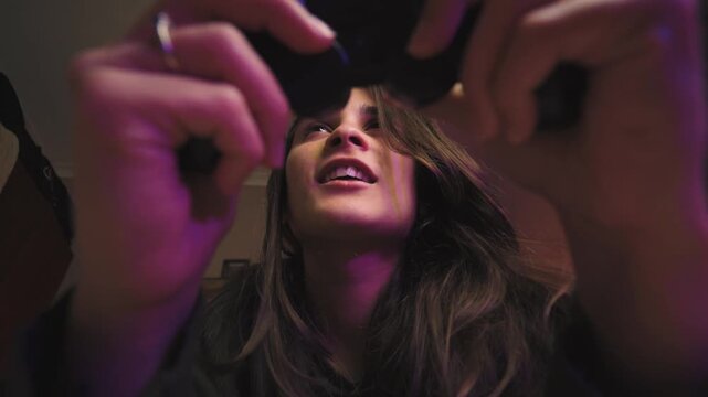 Low-angle shot of a young Hispanic woman playing video games in her bedroom, celebrating an exciting victory. Gaming, fun, success, home entertainment, authentic lifestyle.
