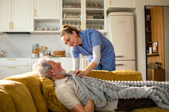 Caregiver tucking in senior man on sofa at home
