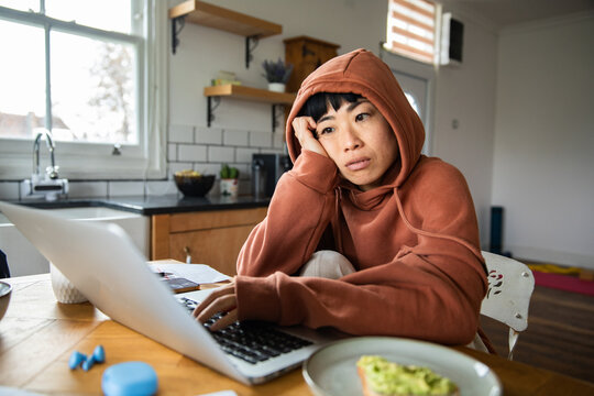 Tired woman working on laptop at kitchen table at home