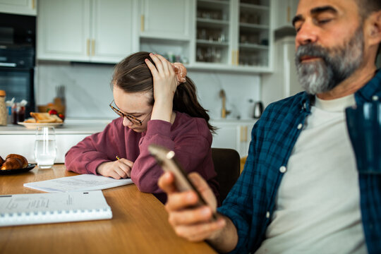 Teen girl studying at kitchen table while parent uses smartphone