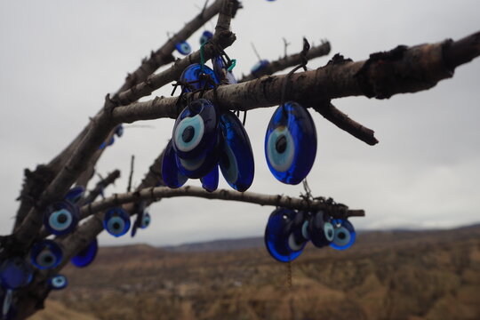 Striking blue glass evil eye (nazar) charms dangle from a bare tree branch above a rugged Anatolian landscape, evoking protection, folk tradition, travel and spiritual belief against the evil eye