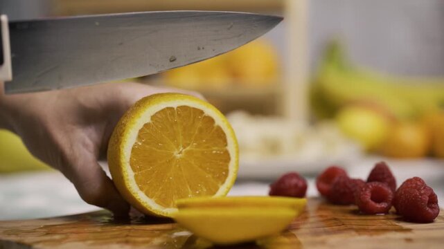 Closeup up of large, sharp knife cutting through juicy orange in kitchen