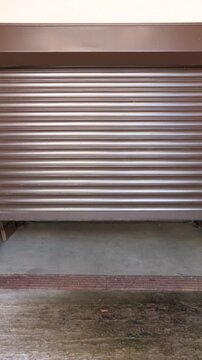 Vertical video blue vintage motorcycle resting inside a garage with its roller shutter partially open, capturing a moment of classic transportation and storage