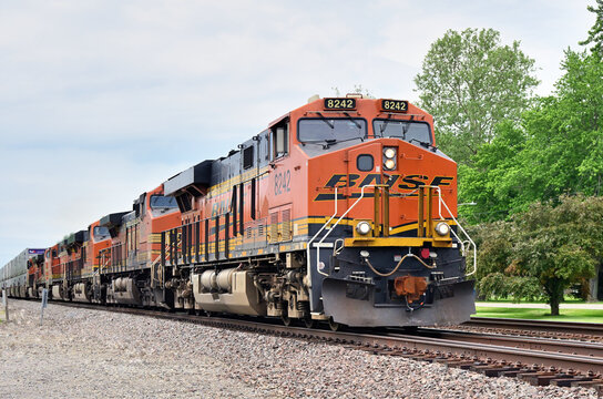 A parade of six Burlington Northern Santa Fe locomotives are on the point of am eastbound stack train passing through a small Illinois community.