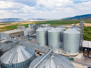 Large storage silos and industrial buildings in a rural area with green fields and cloudy sky © DSMT