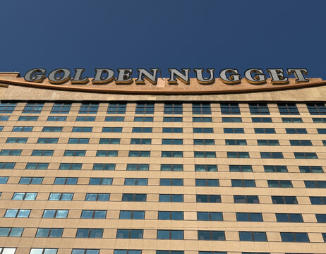Atlantic City's Golden Nugget marquee atop a multi-story hotel facade with repeating window grid and warm stone cladding, photographed under a deep blue sky, evoking urban scale and hospitality.