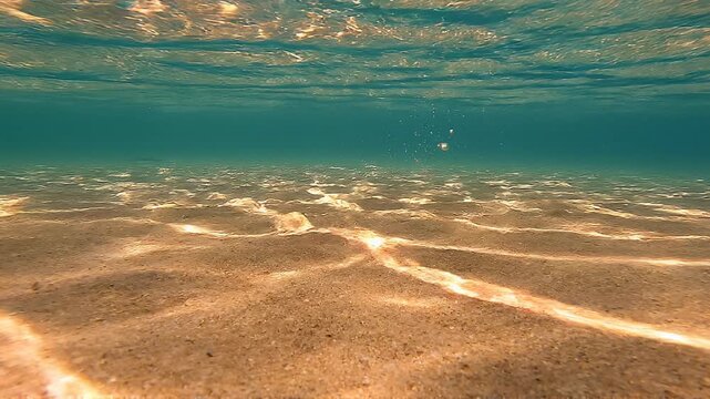 Underwater view of a sandy seabed with sunlight reflections and crystal blue water