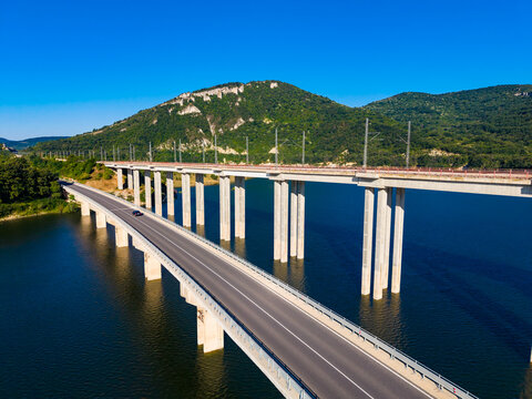 View of a bridge spanning over water with green hills in the background during a clear day