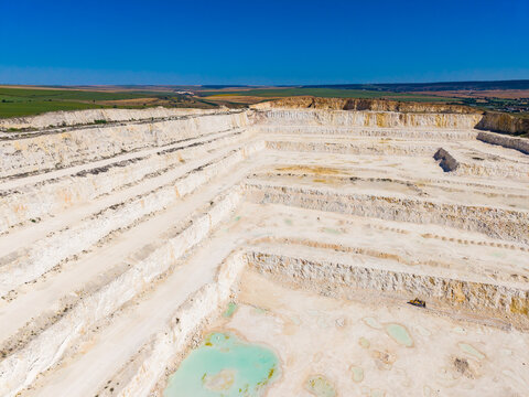 Wide view of a limestone quarry with several layers and small ponds under a clear blue sky