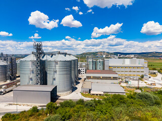 View of grain silos and industrial buildings in a rural area under a clear blue sky with white clouds © DSMT