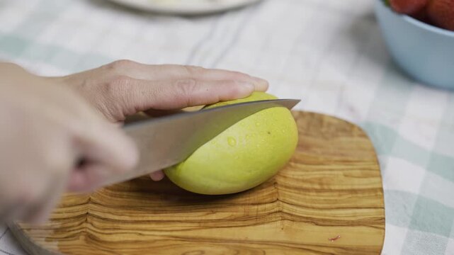 Hands of woman using knife and trying to cut through middle of mango