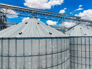 Grain storage silos standing near industrial structures under a blue sky with clouds © DSMT