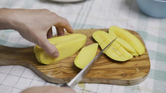 Person using sharp knife to cut up squares into mango slices, closeup