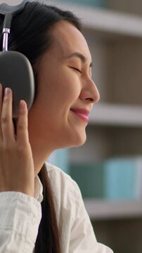 Happy Asian Korean business woman using smartphone headphones listening music joyful student female employee Japanese businesswoman girl office worker mobile phone online wireless audio song indoors