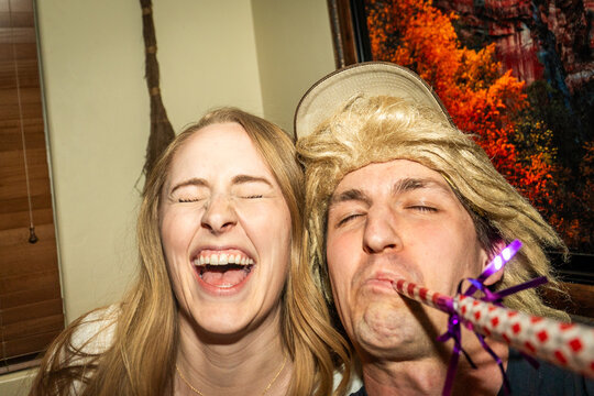 Two smiling friends taking joyful selfie indoors with party horn and festive mood