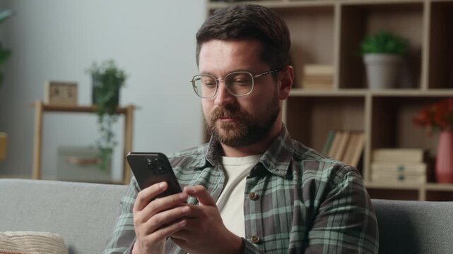Caucasian calm serious relaxed addicted man at home using mobile phone chatting guy male gamer user smartphone device gadget social media shopping online app living room couch sofa browsing internet