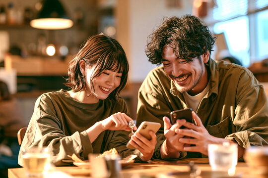 カフェでスマートフォンを見ながら笑顔で会話する若い男女
