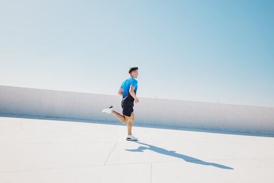 Runner enjoys bright sunlit day while jogging on a rooftop against a clear blue sky