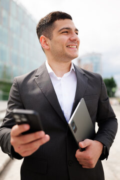 Confident business professional smiles while holding a phone and tablet in a modern urban setting