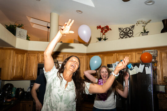 Indoor celebration with balloons, raised hands, cheerful kitchen gathering