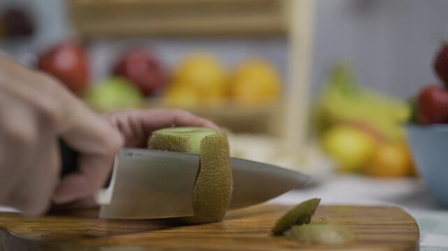 Knife cutting off skin of kiwi on cutting board in kitchen - low, closeup shot