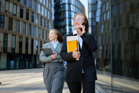 Business women walking confidently in a modern city with colorful folders and tablets in their hands