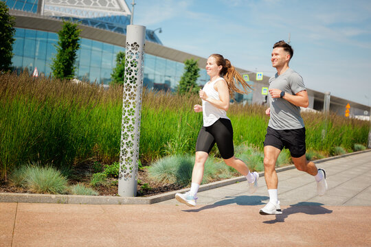 Joyful couple runs together in a bright urban park under a clear blue sky