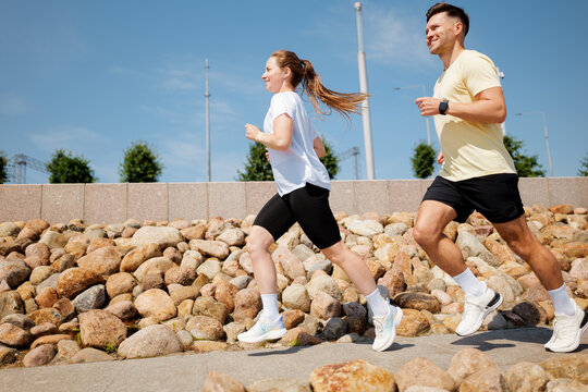 Couple enjoys a sunny morning jog along a rocky path near a park