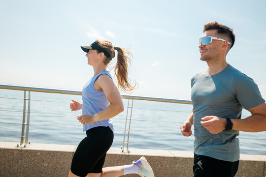 Couples jog along the waterfront, enjoying the sun and the refreshing breeze of a bright day at the seaside