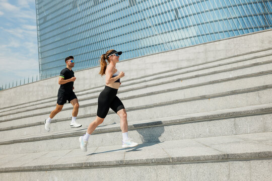 Two fitness enthusiasts ascend polished steps under a bright blue sky in a modern urban setting