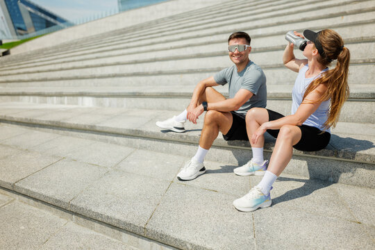 Two friends enjoying a refreshing break on outdoor steps after an energizing workout in a vibrant city