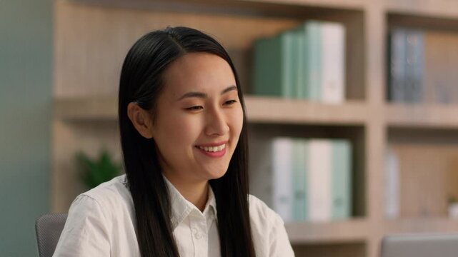 Happy Asian Japanese office manager business woman talking video call on laptop positive worker Chinese Korean female businesswoman girl looking computer screen smiling online virtual discuss indoors