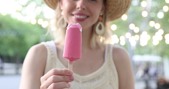 Happy woman in hat eating delicious ice pop in park. Camera moving backwards
