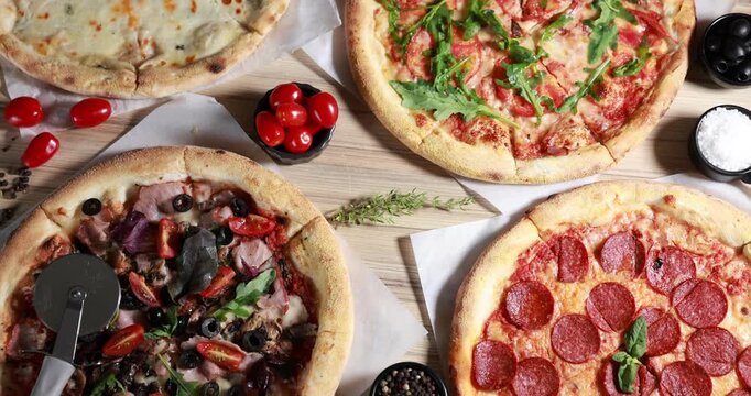 Different yummy pizzas, ingredients and cutter on wooden table, flat lay