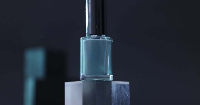 Nail polish in bottle on podium against dark background, closeup. Camera moving up