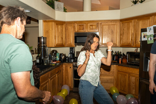 Adults dancing in kitchen during lively home celebration with balloons