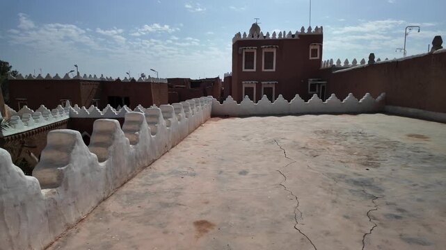 Ushaiqer Heritage Village traditional Najdi mud-brick architecture, with ancient buildings and thriving date palm trees standing under blue sky, illustrating historical Arabian life of Saudi Arabia