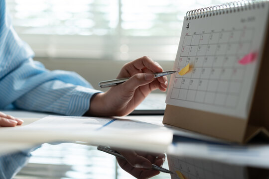 Businesswoman marking important dates on desktop calendar with pen, representing business planning, project scheduling, deadline management, appointment organization and productivity.