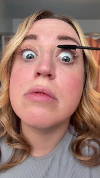 woman applying mascara to her eyelashes and flinching