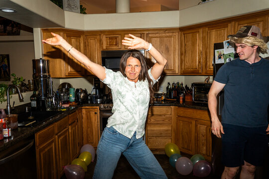 Woman dancing with raised arms in bright kitchen during playful home party