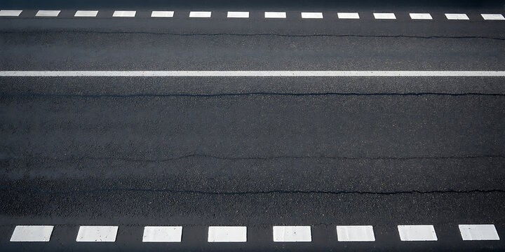 Overhead view of a dark asphalt road with a white solid line and dashed white lines indicating