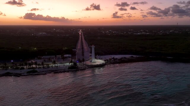 Aerial drone flight orbiting illuminated lighthouse at Mahahual beach during dusk in Mexico