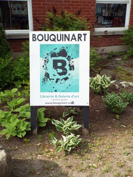 Gatineau,Quebec, Canada &ndash; June 4, 2026: The "Bouquinart" sign for a librairie and galerie d'art stands in a garden bed with hostas near a brick building on rue Principale.