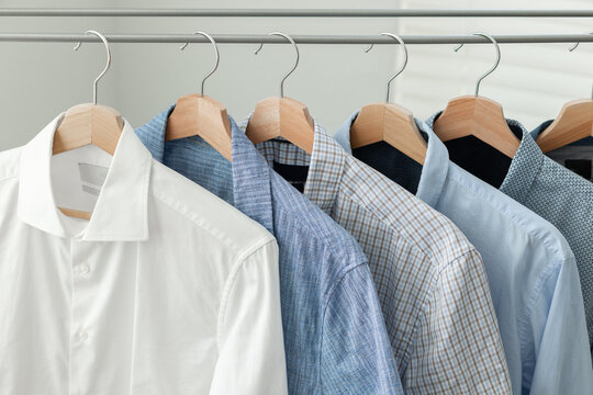 A row of blue-toned casual shirts hanging on wooden hangers on a folding clothes drying rack. Cleaning and organization. Laundry Day.
