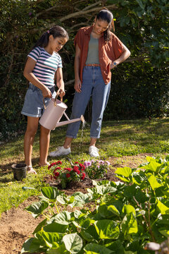 African mother and child watering red and purple flowers in backyard with pale pink watering can