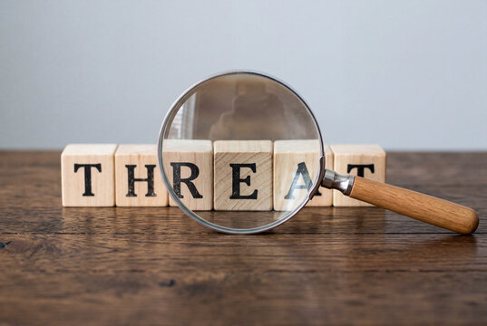 Magnifying glass focusing on wooden blocks spelling the word threat on a dark wooden table