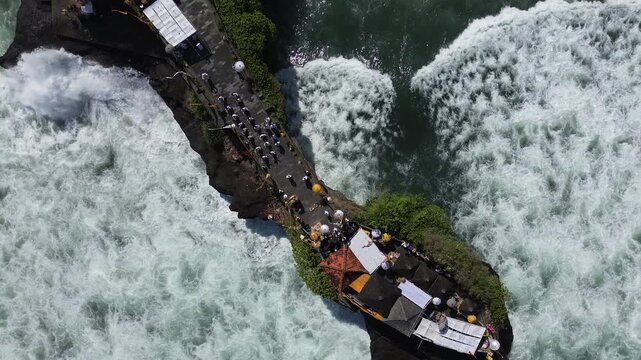 Aerial view of a narrow coastal path between crashing waves, Aerial view of a narrow coastal path between crashing waves. Tourists walk along a rocky promenade above the ocean. Bright sunlight reflect