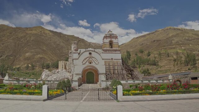 Vertical tilt-up shot from plaza entrance to damaged facade and bell tower of Purisima Concepcion church in Lari, Colca Valley, Arequipa, Peru.